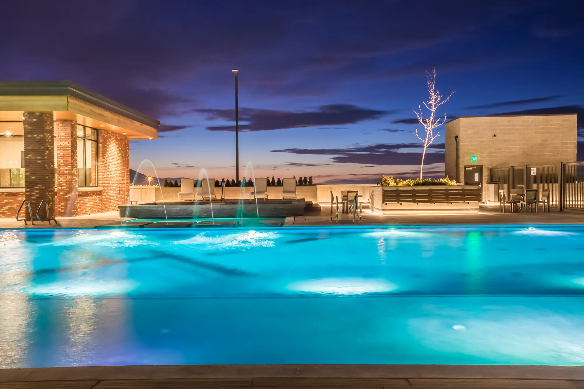 The 4th West rooftop pool lit at night, fountains arcing over the glowing water