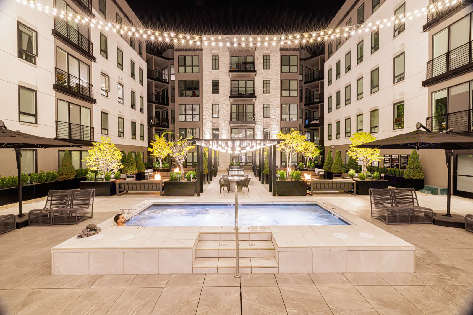 The Sugar Alley courtyard spa at night, string lights strung overhead and a resident in the lit water